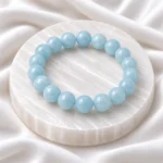 Aquamarine Crystal Bracelet with polished light blue round gemstone beads displayed on a white selenite plate.