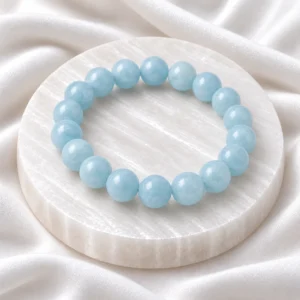 Aquamarine Crystal Bracelet with polished light blue round gemstone beads displayed on a white selenite plate.