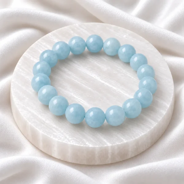Aquamarine Crystal Bracelet with polished light blue round gemstone beads displayed on a white selenite plate.