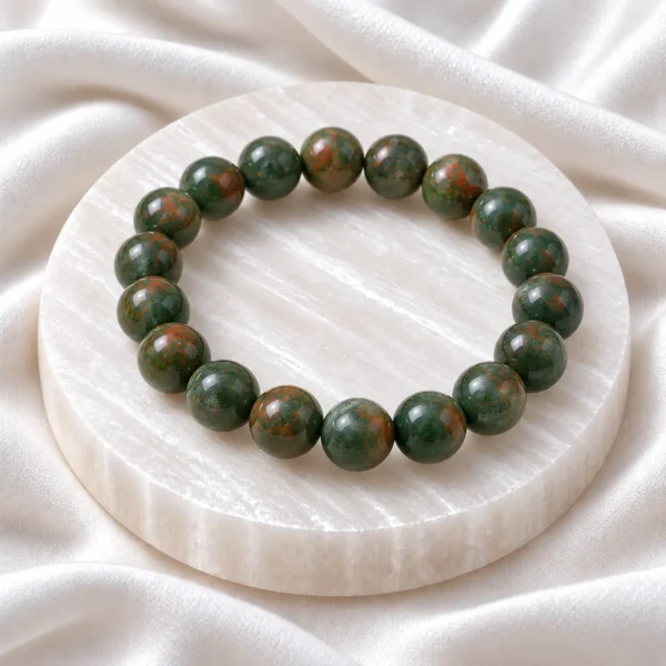 Natural Bloodstone Crystal Bracelet with polished dark green round gemstone beads featuring reddish-brown spots, displayed on a white selenite plate.