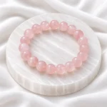 Natural Rose Quartz Crystal Bracelet with polished light pink round gemstone beads displayed on a white crystal plate.