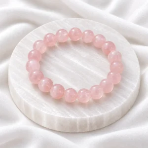 Natural Rose Quartz Crystal Bracelet with polished light pink round gemstone beads displayed on a white crystal plate.