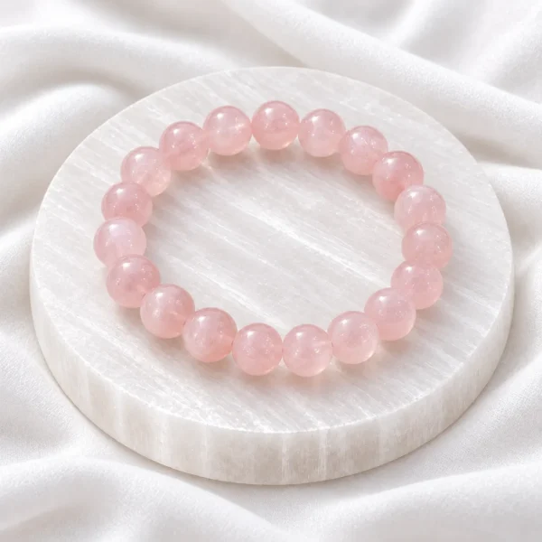 Natural Rose Quartz Crystal Bracelet with polished light pink round gemstone beads displayed on a white crystal plate.