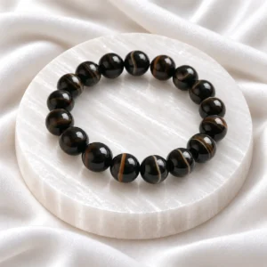 Natural Black Agate Crystal Bracelet with polished round black and brown banded Sulemani Hakik gemstone beads displayed on a white selenite plate.