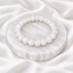 White Selenite Crystal Bracelet with round polished beads displayed on a circular selenite plate over soft white fabric.
