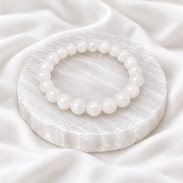 White Selenite Crystal Bracelet with round polished beads displayed on a circular selenite plate over soft white fabric.