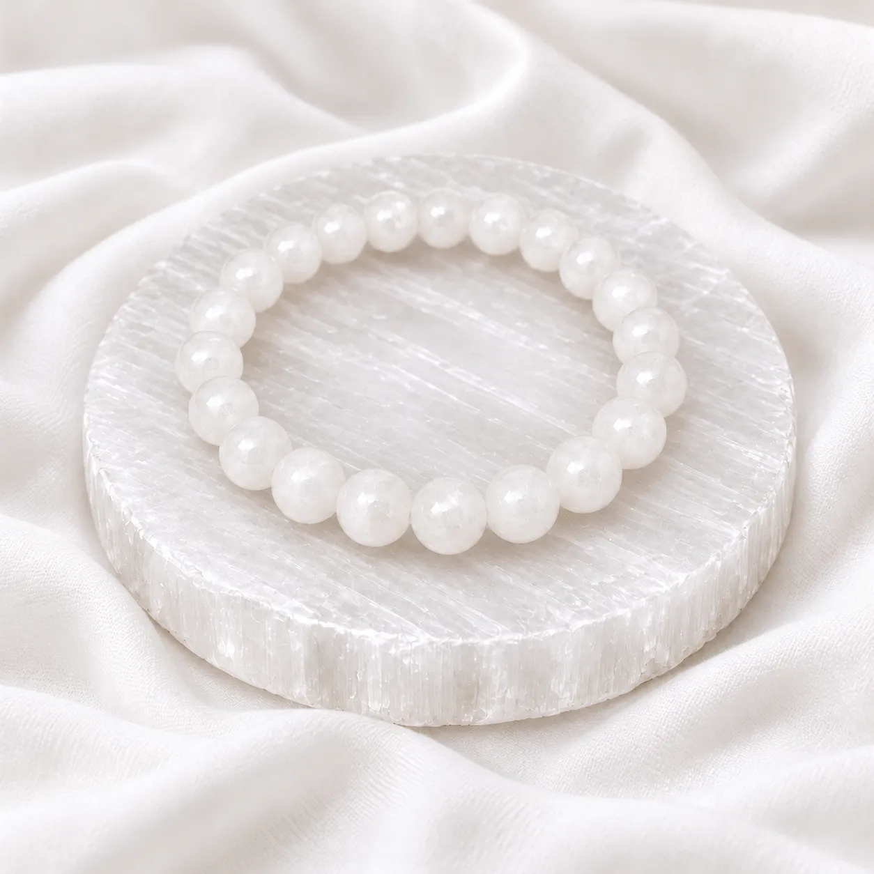Selenite Crystal Bracelet (2) White Selenite Crystal Bracelet with round polished beads displayed on a circular selenite plate over soft white fabric.