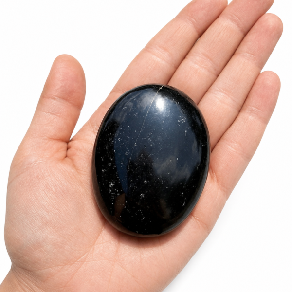 Natural Black Tourmaline Palm Stone / Worry Stone held in a human hand on a clean white background.