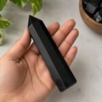 Black Obsidian crystal point held in a hand, showing its polished faceted surface