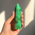 Natural green chrysoprase crystal pencil obelisk tower held in hand, showing vibrant green color and natural brown matrix patterns