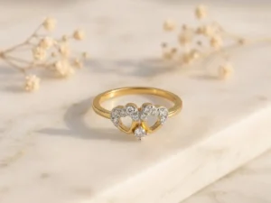 Gold ring featuring two interlocking heart shapes adorned with small sparkling diamonds on a minimalist light background.