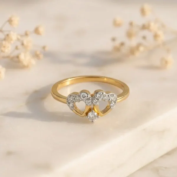 Gold ring featuring two interlocking heart shapes adorned with small sparkling diamonds on a minimalist light background.