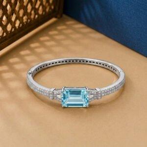 A white gold Art Deco bangle featuring a central emerald-cut blue stone and pavé diamonds on a neutral background.