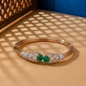 A yellow gold architectural bangle featuring a central emerald-cut green stone and pavé diamonds on a neutral background.