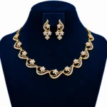 Yellow gold floral wave lab grown diamond necklace set with round diamond flower motifs and matching floral drop earrings on navy blue display