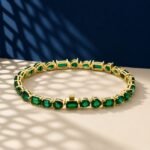 A professional macro photo of an emerald multi shape tennis bracelet with mixed-cut green stones in yellow gold