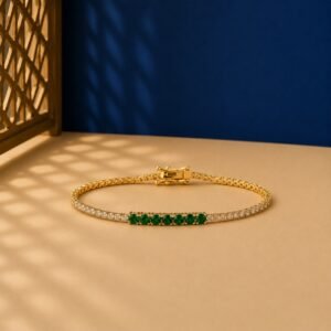 Seven-stone emerald accent lab-grown diamond tennis bracelet in a yellow-toned metal setting on a two-toned background.