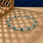 Cushion-cut lab emerald infinity bracelet with diamond halos in white metal.