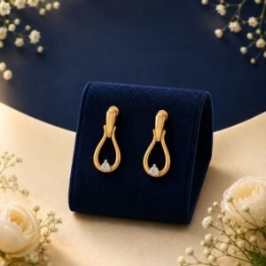 Pair of 18K yellow gold open teardrop drop earrings with a cluster of lab-grown diamonds displayed on a navy blue velvet jewelry stand surrounded by white flowers.
