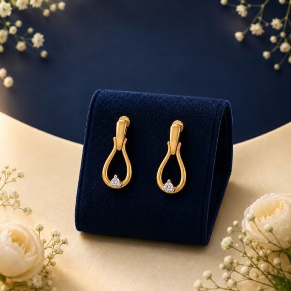 Pair of 18K yellow gold open teardrop drop earrings with a cluster of lab-grown diamonds displayed on a navy blue velvet jewelry stand surrounded by white flowers.