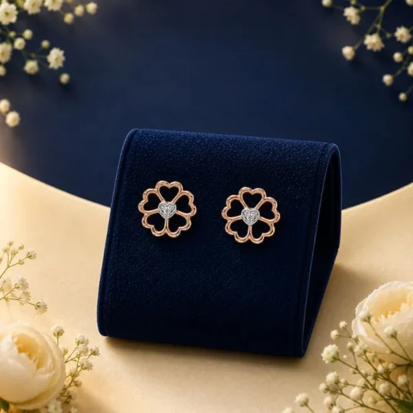 Pair of 18K rose gold five-petal flower cutout stud earrings featuring a heart-shaped lab-grown diamond at the center, displayed on a navy blue velvet mount.
