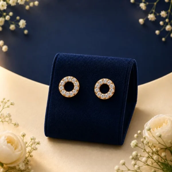 Pair of 18K yellow gold open circle stud earrings featuring a continuous eternity loop of pave white lab-grown diamonds, displayed on a blue velvet mount.