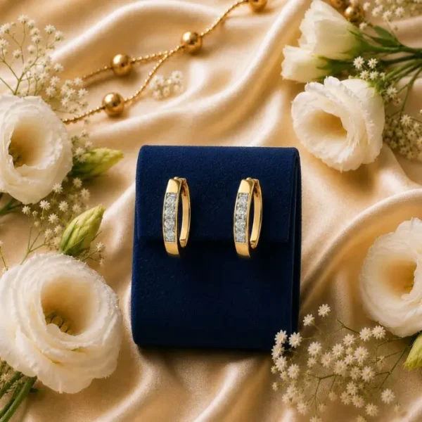 Pair of 14k gold lab-grown diamond channel-set huggie hoop earrings displayed on a blue velvet box surrounded by white flowers.