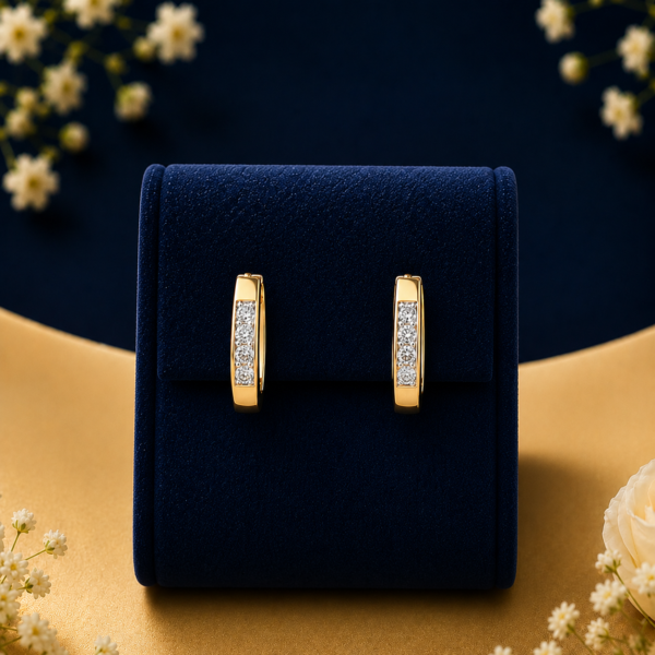 Pair of 14k gold lab-grown diamond channel-set huggie hoop earrings displayed on a blue velvet box surrounded by white flowers.