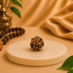 Close-up of an original natural 3 Mukhi Rudraksha bead displayed on a white platform with a premium spiritual-themed background.