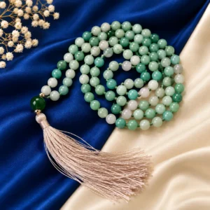 Crystal Mala with polished green and white gemstone beads, silver-toned accents and a cream tassel displayed on blue and cream silk fabric.