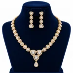 18K gold trillion cut lab grown diamond halo necklace set with triangular diamond motifs, central dangling pendant and matching earrings on navy blue jewellery bust