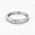 Angled view of Regal Emerald Moissanite Men's Ring showcasing a silver band, emerald-cut Moissanite gemstone and textured finish.
